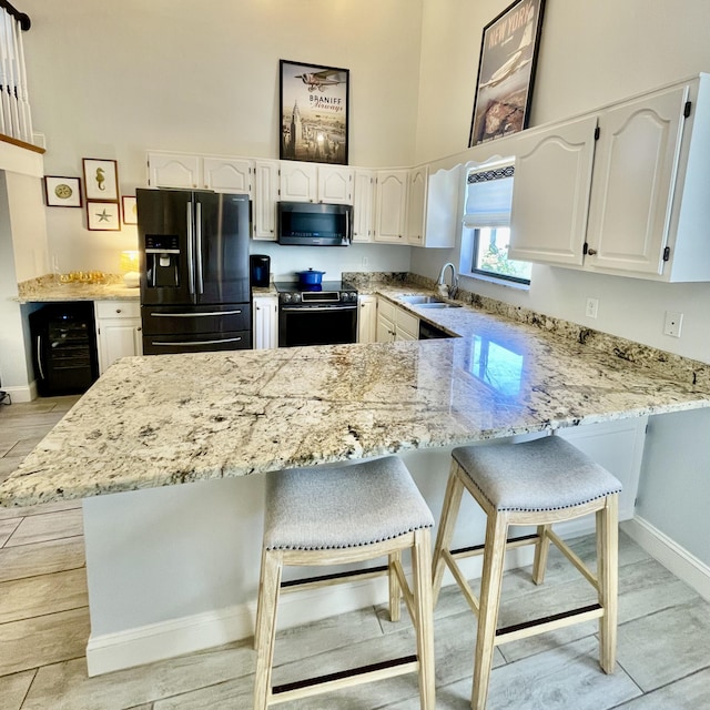 kitchen with black fridge with ice dispenser, a breakfast bar area, kitchen peninsula, range with electric stovetop, and sink