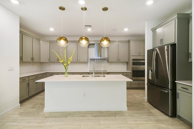 kitchen with appliances with stainless steel finishes, a center island with sink, pendant lighting, and wall chimney range hood