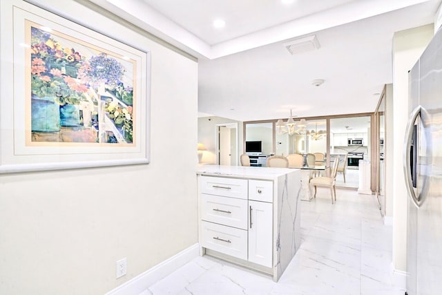 kitchen featuring kitchen peninsula, a notable chandelier, stainless steel refrigerator, and white cabinetry