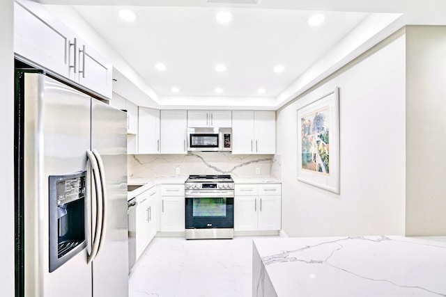 kitchen with white cabinets, stainless steel appliances, backsplash, light stone counters, and a tray ceiling