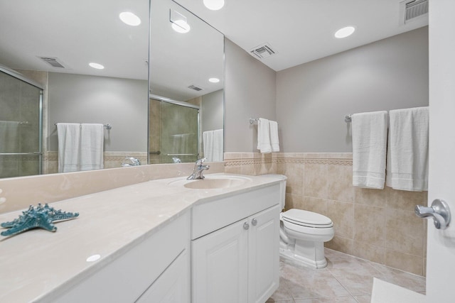 bathroom with toilet, tile walls, vanity, a shower with door, and tile patterned flooring