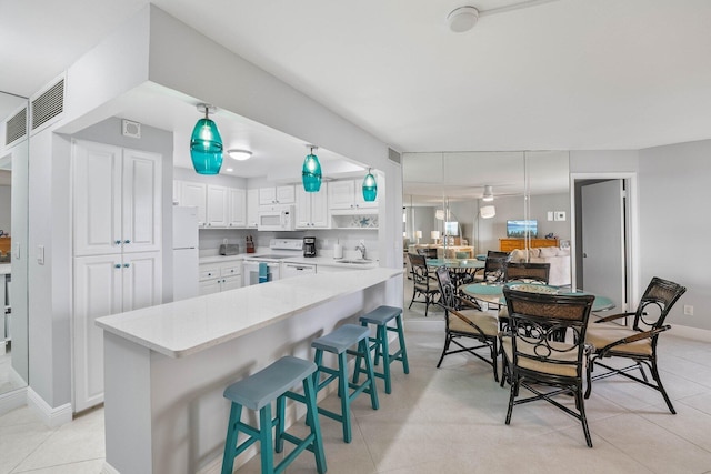 kitchen with light tile patterned floors, white appliances, white cabinets, a kitchen bar, and decorative light fixtures