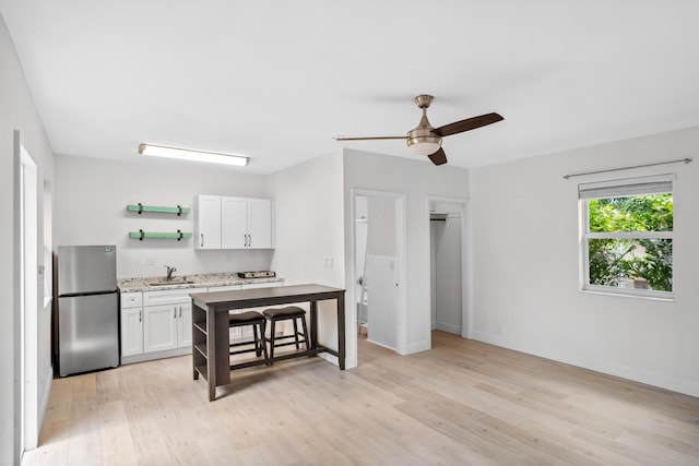 kitchen featuring white cabinetry, sink, ceiling fan, stainless steel fridge, and light hardwood / wood-style floors