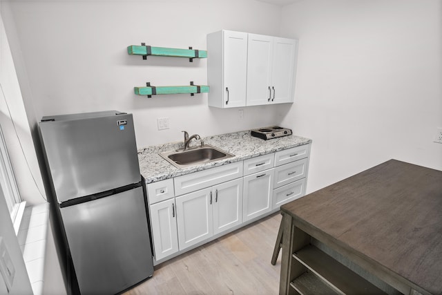 kitchen featuring stainless steel fridge, light stone counters, sink, light hardwood / wood-style flooring, and white cabinets