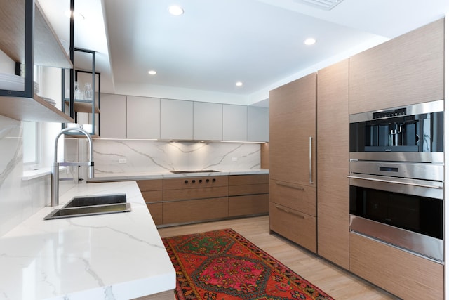 kitchen with gray cabinetry, light hardwood / wood-style flooring, double oven, light stone counters, and tasteful backsplash