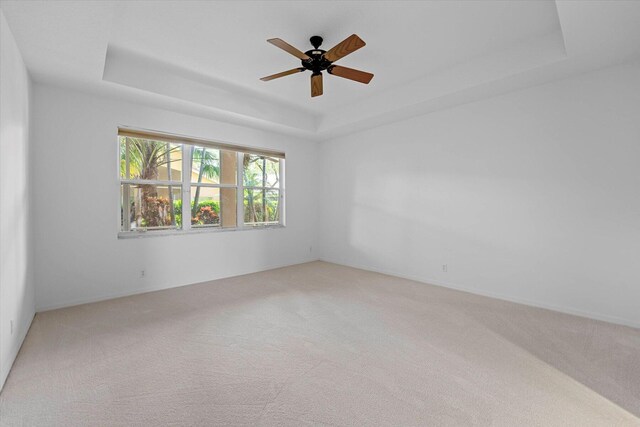 carpeted empty room featuring ceiling fan and a raised ceiling