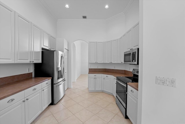 kitchen featuring white cabinets, appliances with stainless steel finishes, light tile patterned floors, and ornamental molding