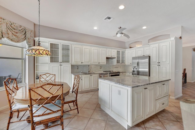 kitchen with ceiling fan, light stone countertops, decorative light fixtures, a kitchen island, and appliances with stainless steel finishes