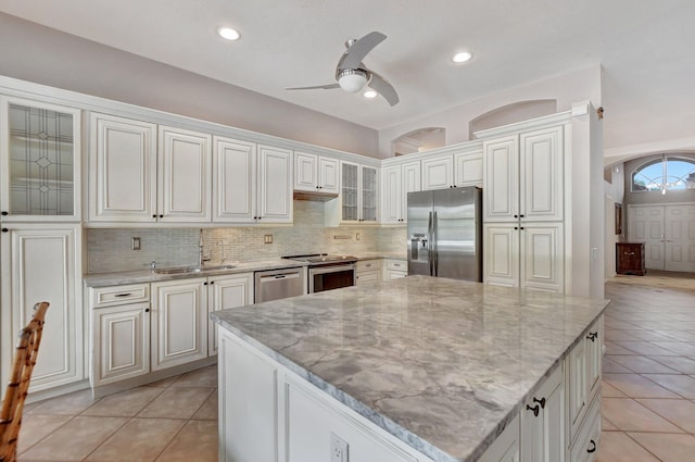 kitchen with sink, a center island, stainless steel appliances, light stone counters, and white cabinets