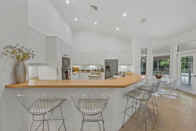 kitchen featuring kitchen peninsula, a towering ceiling, a breakfast bar, white cabinets, and appliances with stainless steel finishes