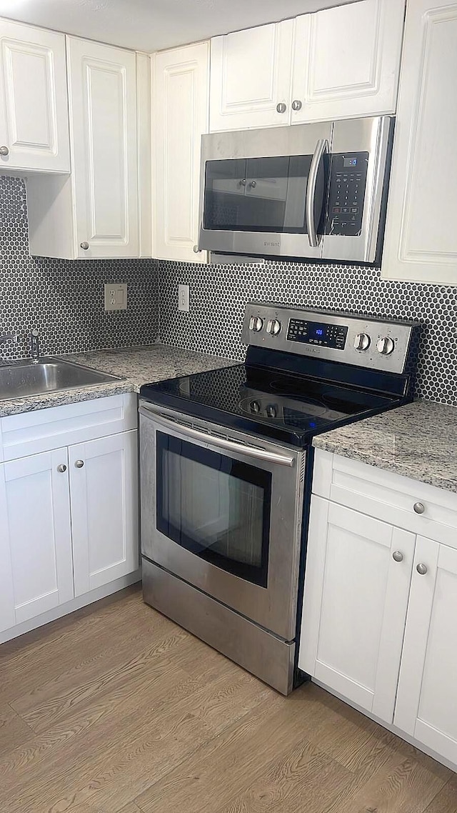 kitchen with appliances with stainless steel finishes, backsplash, white cabinetry, and light hardwood / wood-style flooring