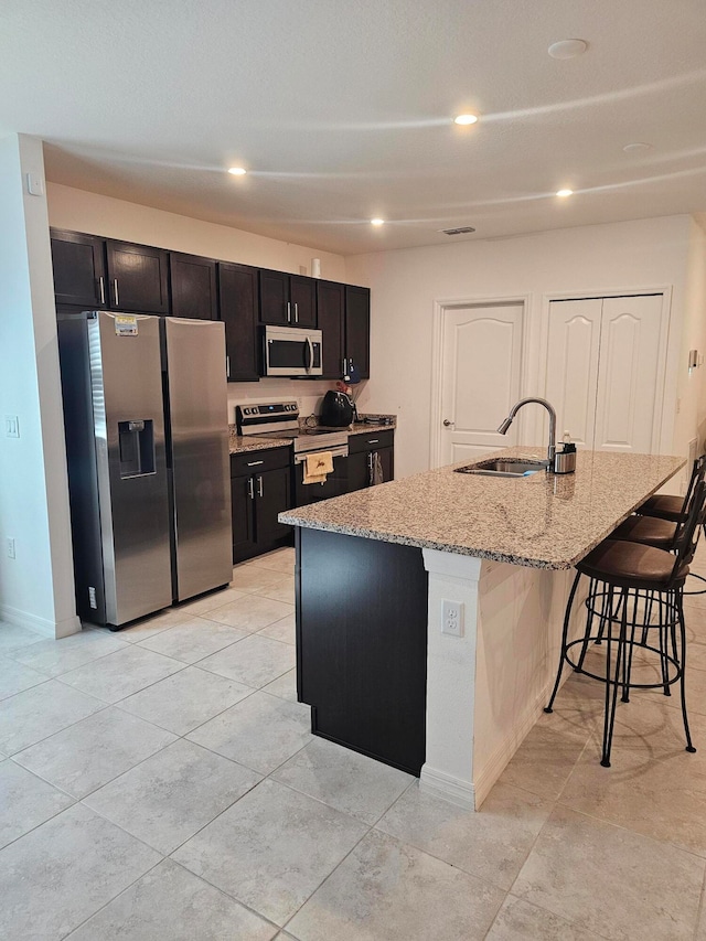 kitchen with a center island with sink, stainless steel appliances, a breakfast bar area, sink, and light tile floors