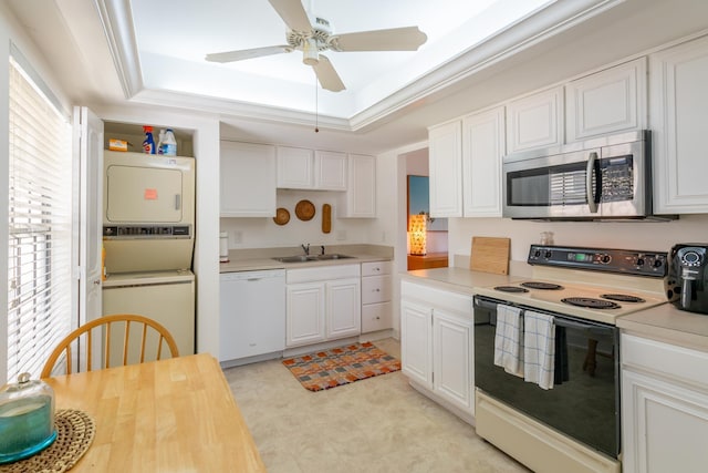 kitchen featuring white cabinets, stacked washer / drying machine, white appliances, and a tray ceiling