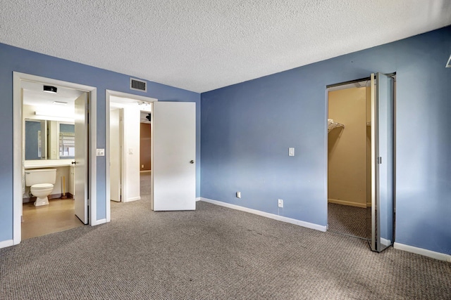 unfurnished bedroom featuring a textured ceiling, a closet, connected bathroom, a spacious closet, and carpet flooring