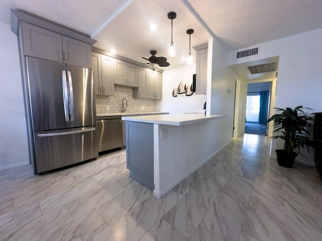 kitchen featuring kitchen peninsula, hanging light fixtures, gray cabinetry, stainless steel appliances, and tasteful backsplash