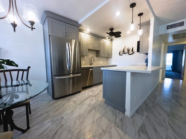 kitchen with decorative backsplash, hanging light fixtures, gray cabinetry, stainless steel appliances, and a textured ceiling