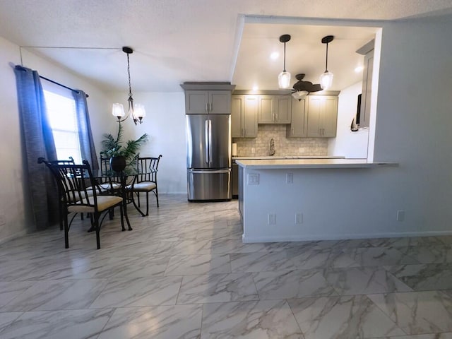 kitchen with kitchen peninsula, backsplash, stainless steel refrigerator, pendant lighting, and gray cabinetry