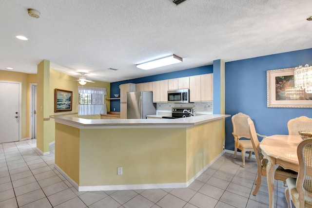 kitchen with appliances with stainless steel finishes, light tile flooring, ceiling fan with notable chandelier, and kitchen peninsula