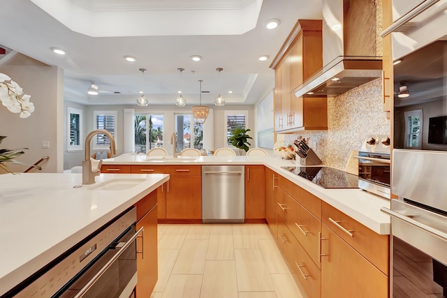 kitchen with sink, wall chimney exhaust hood, black electric cooktop, a tray ceiling, and decorative light fixtures