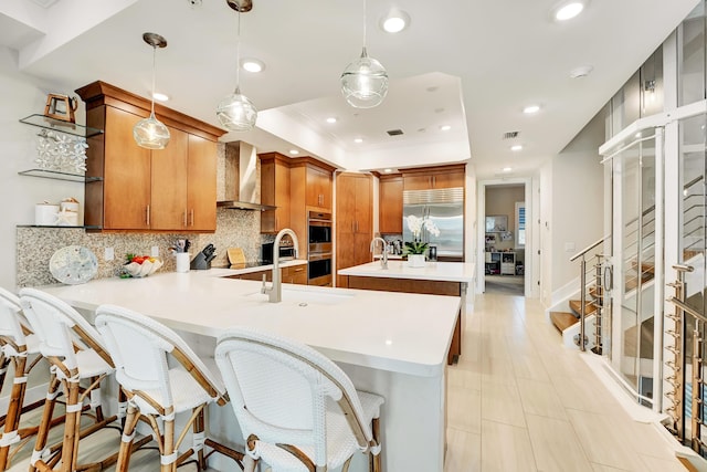 kitchen featuring a breakfast bar, wall chimney range hood, decorative light fixtures, kitchen peninsula, and stainless steel appliances