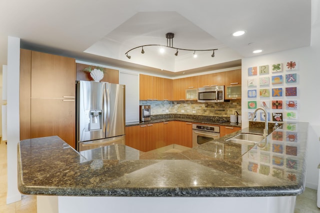 kitchen featuring sink, kitchen peninsula, dark stone counters, decorative backsplash, and appliances with stainless steel finishes