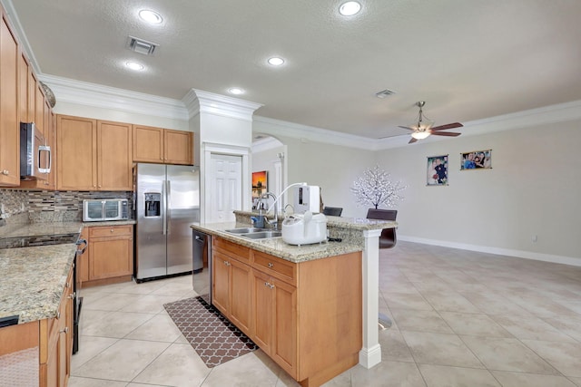 kitchen with ceiling fan, sink, stainless steel appliances, an island with sink, and ornamental molding