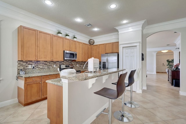 kitchen featuring light stone countertops, decorative backsplash, a center island with sink, appliances with stainless steel finishes, and ornamental molding