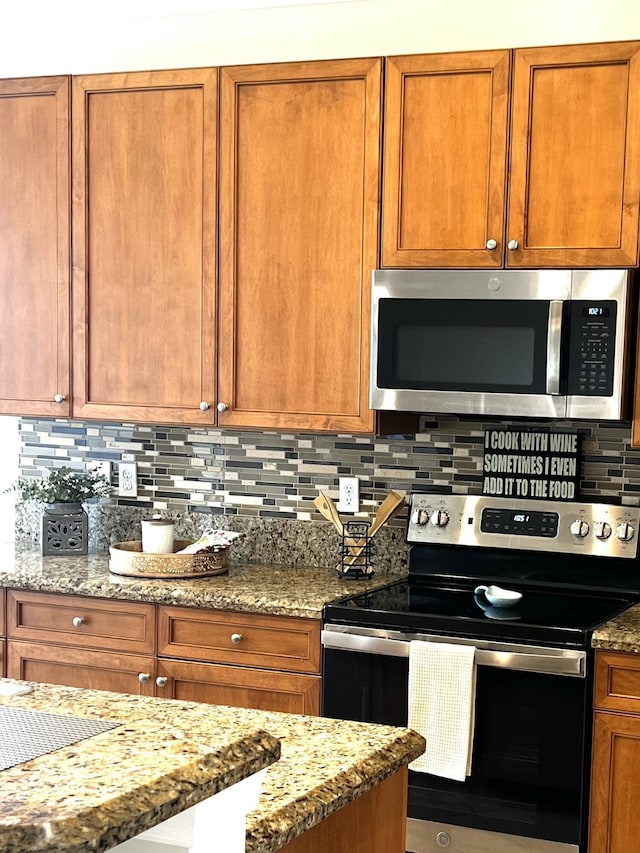 kitchen with decorative backsplash, light stone countertops, stainless steel appliances, and brown cabinetry