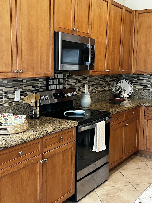 kitchen featuring brown cabinetry, dark stone countertops, and appliances with stainless steel finishes