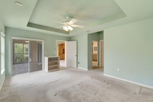 unfurnished bedroom featuring ceiling fan, a tray ceiling, light colored carpet, and ensuite bathroom