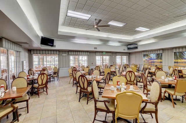 tiled dining space with ceiling fan and a tray ceiling