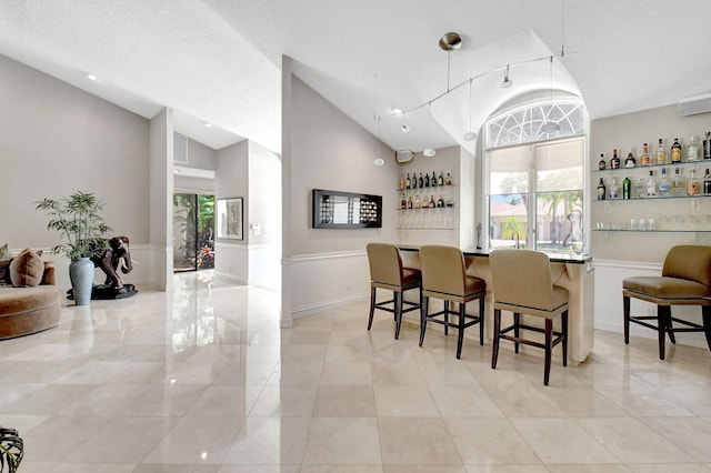 bar with a healthy amount of sunlight, light tile patterned floors, a textured ceiling, and high vaulted ceiling