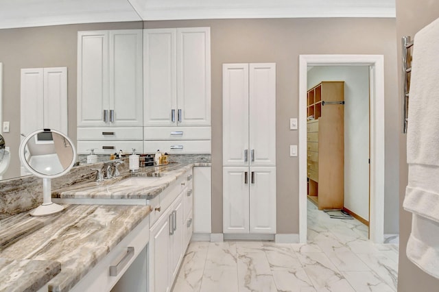 kitchen with white cabinets, ornamental molding, sink, and light stone counters