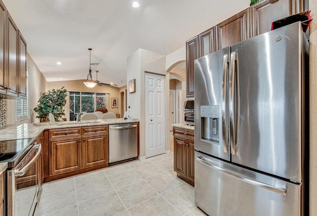 kitchen featuring appliances with stainless steel finishes, lofted ceiling, decorative light fixtures, kitchen peninsula, and light stone counters