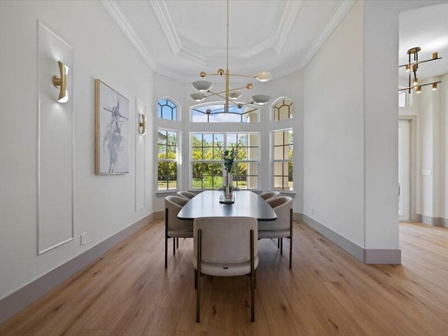 dining area featuring a raised ceiling, light wood-type flooring, ornamental molding, and an inviting chandelier