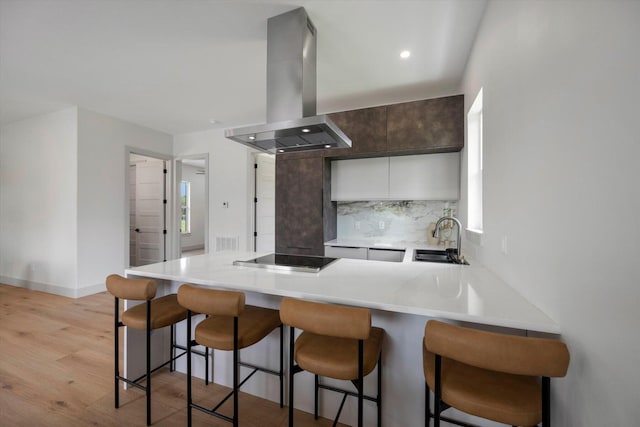 kitchen featuring sink, black electric cooktop, light hardwood / wood-style floors, kitchen peninsula, and island exhaust hood