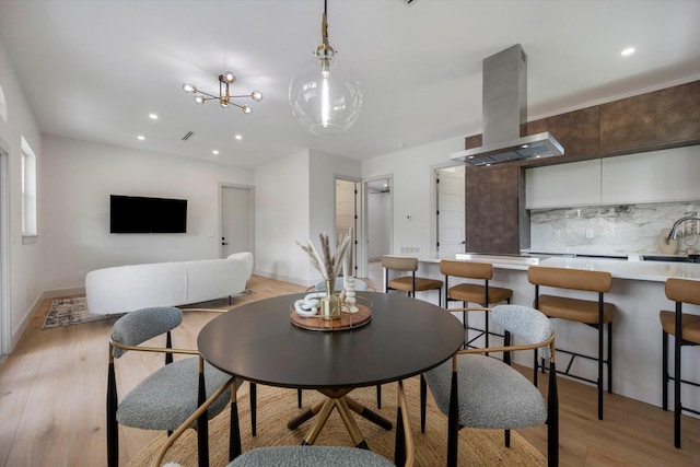 dining space with a notable chandelier, sink, and light hardwood / wood-style flooring