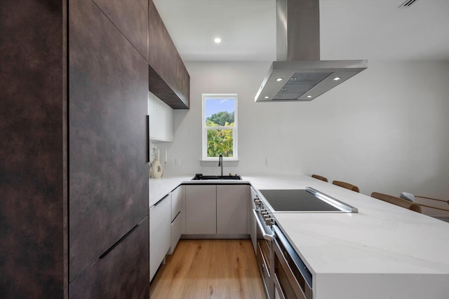 kitchen featuring kitchen peninsula, light wood-type flooring, wall chimney exhaust hood, sink, and fridge