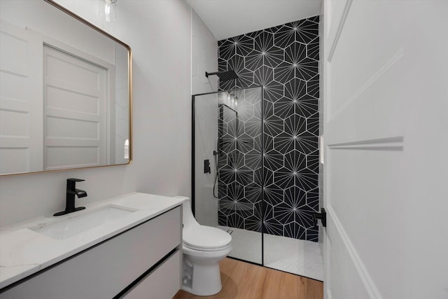 bathroom with tiled shower, vanity, hardwood / wood-style flooring, and toilet