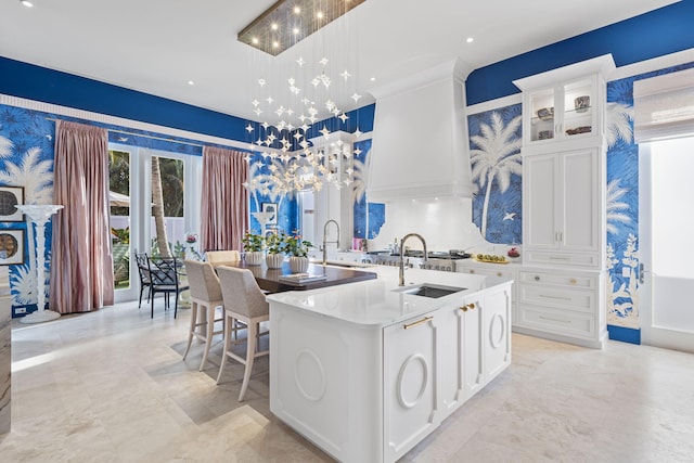 kitchen featuring an island with sink, sink, white cabinets, and decorative light fixtures