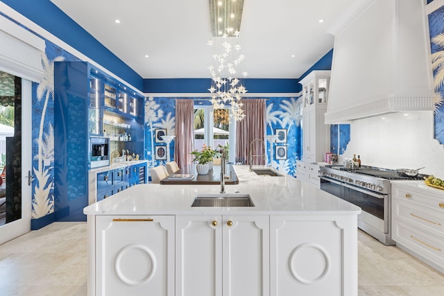 kitchen with hanging light fixtures, an island with sink, white cabinets, and range with two ovens