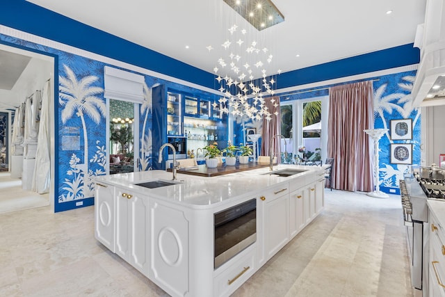 kitchen featuring sink, decorative light fixtures, white cabinets, and a center island with sink