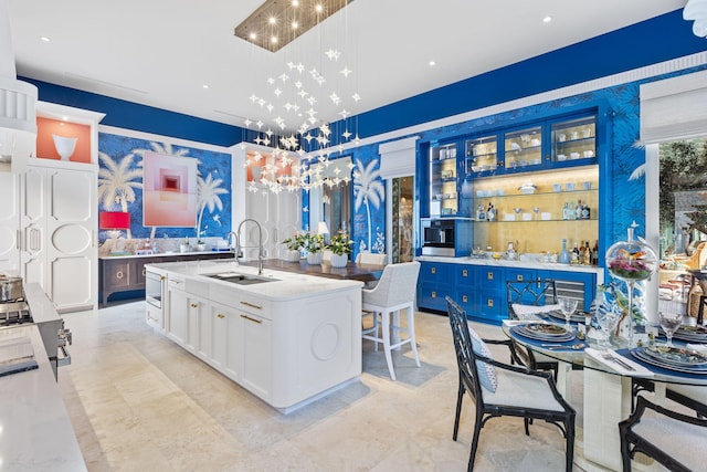 kitchen featuring decorative light fixtures, blue cabinets, white cabinetry, sink, and a kitchen island with sink