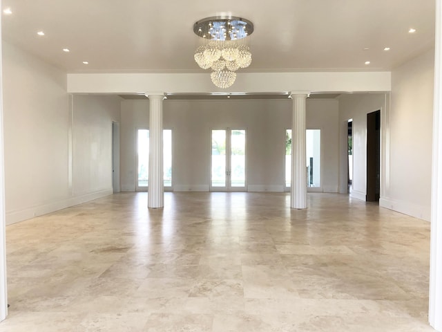 empty room with french doors, decorative columns, and a notable chandelier