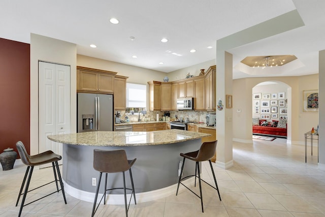 kitchen featuring light stone countertops, stainless steel appliances, a tray ceiling, a center island, and a breakfast bar area