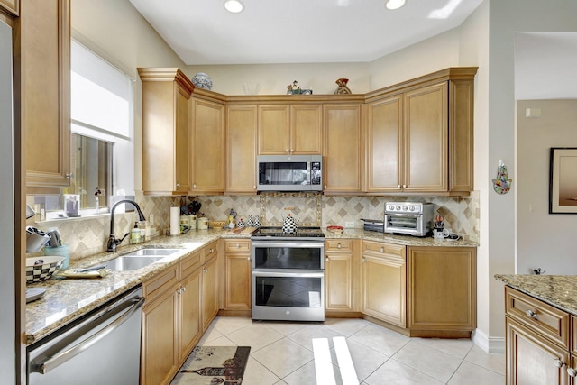 kitchen with appliances with stainless steel finishes, tasteful backsplash, light stone counters, sink, and light tile patterned flooring