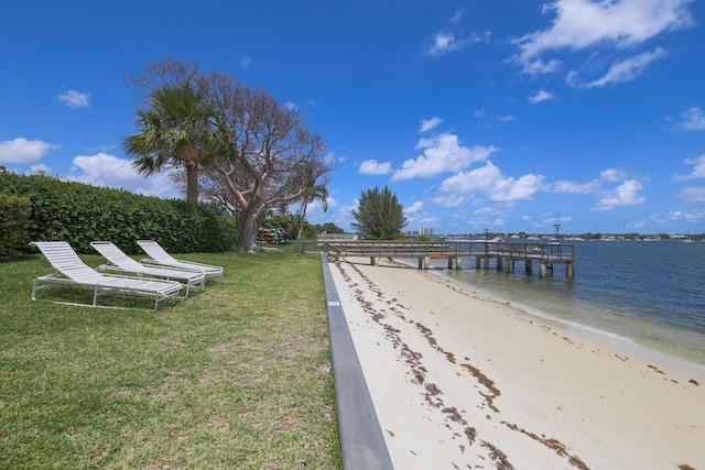 view of dock with a water view, a beach view, and a yard