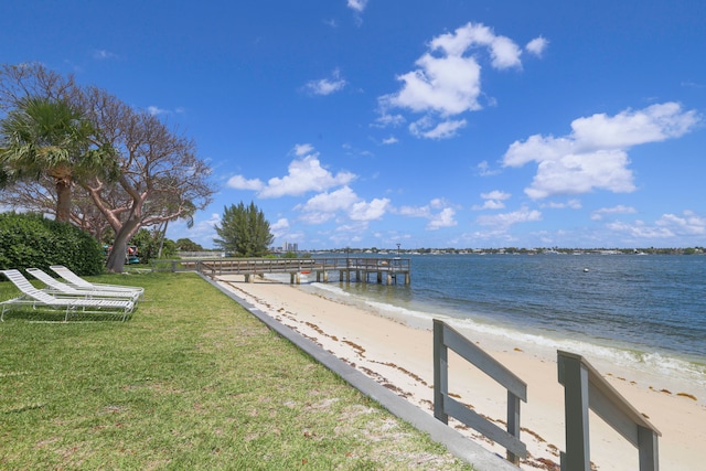 dock area with a yard, a water view, and a view of the beach