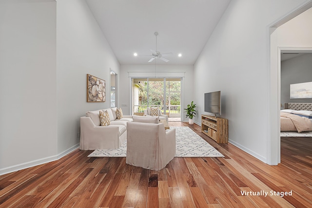 living room featuring high vaulted ceiling, a ceiling fan, baseboards, and wood finished floors