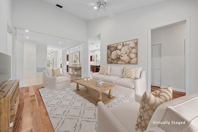 living room featuring a towering ceiling, a ceiling fan, visible vents, and wood finished floors